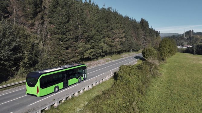 Turystyczny autobus sunie autostradą przez zielone pola i wzgórza Europy z górami w oddali