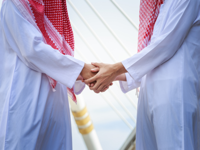 Grupa arabskich biznesmenów w thobe i ghutra siedzi przy stole w sali konferencyjnej